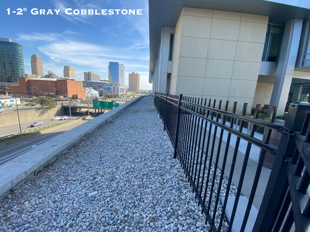 Gray cobblestone in a landscape bed next to a fence in Kansas City