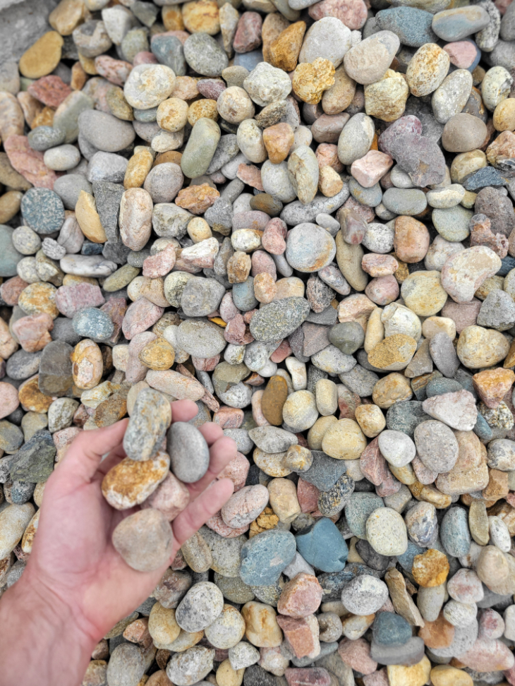 close up photo of multi colored cobblestone in the palm of a hand