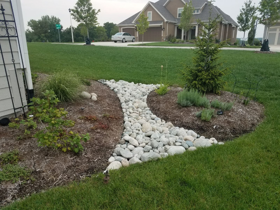 Gray Cobblestone in a landscape bed to control water flow surrounded by plants