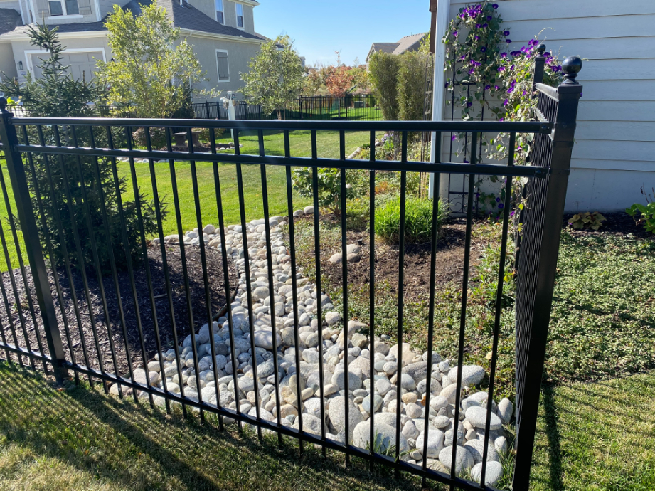 Gray cobblestone near a fence in a sloped landscape area to control water flow located in Kansas City